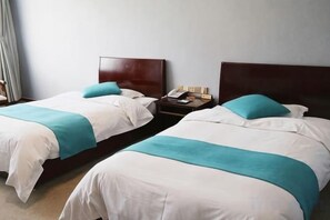 Two twin beds with wooden headboards, a bedside table with a lamp, and a wall-mounted telephone. - Xincheng Hotel (Yiyuan)