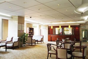 A hotel lobby with multiple seating areas, a reception desk, and a large potted plant. - Xincheng Hotel (Yiyuan)