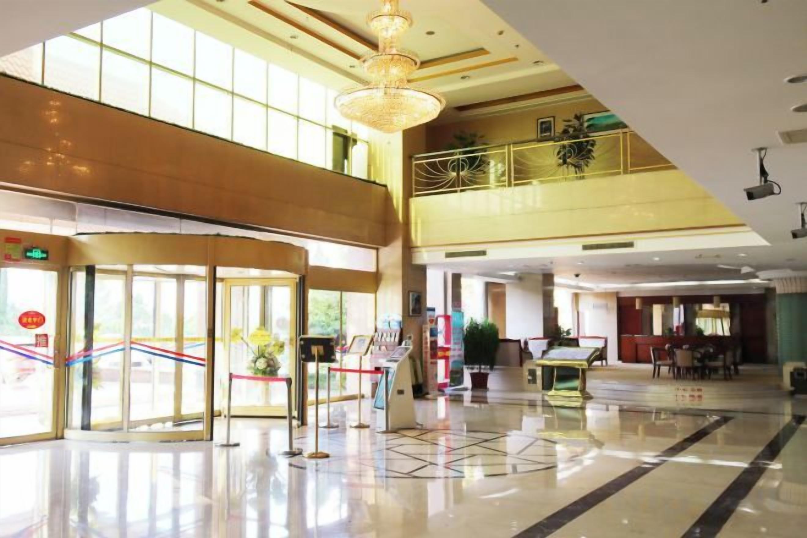 Een hotel lobby met een glazen ingang, een receptiebalie en een trap naar een hoger niveau.