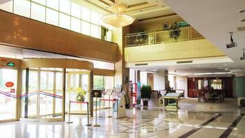 Een hotel lobby met een glazen ingang, een receptiebalie en een trap naar een hoger niveau.