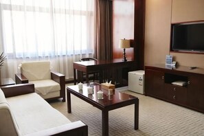 Ein Hotelzimmer mit einem Bett, einem Schreibtisch, einem Sessel, einem Fernseher und einem kleinen Kühlschrank.