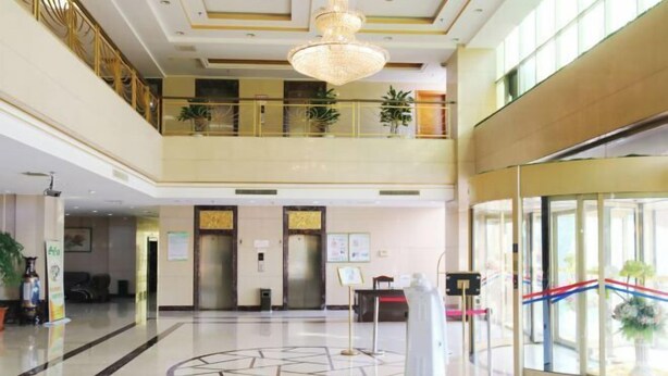 A spacious lobby with a high ceiling, a chandelier, a reception desk, and a glass elevator.