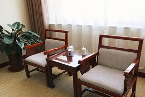 A room with two wooden chairs and a small table, a potted plant, and a window with curtains. - Xincheng Hotel (Yiyuan)