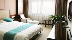 A hotel room with a large bed, a desk, a chair, a TV, and a window with curtains.