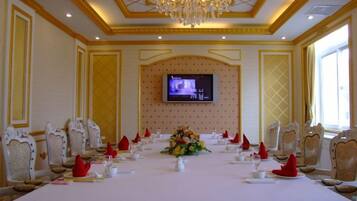 A conference room with a long table, chairs, a chandelier, and a television screen.