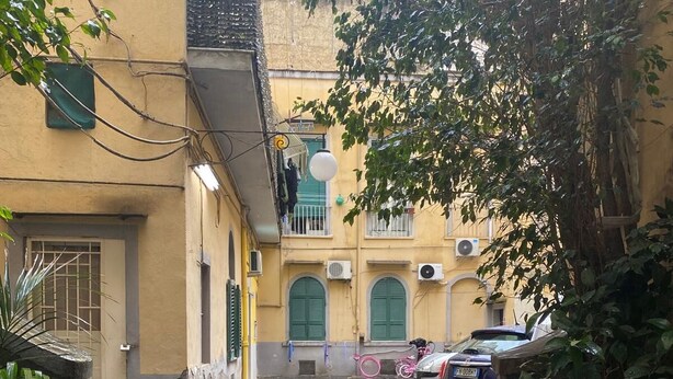 A narrow street with wet cobblestone pavement, yellow buildings, and parked cars. - Stay Costa House Naples (Naples)