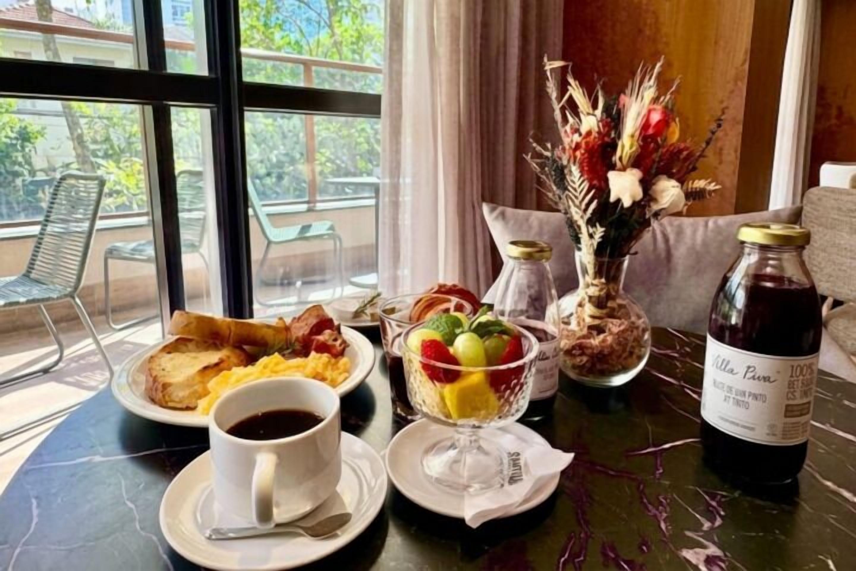 A breakfast setting with a table, a vase of flowers, and a bottle of wine.