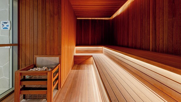 Un sauna aux murs et aux bancs en bois, une table en bois ornée de pierres et un sol carrelé.