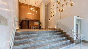 Un hall d’hôtel moderne avec un escalier en marbre, un comptoir d’accueil et un escalier doté d’une main courante.
