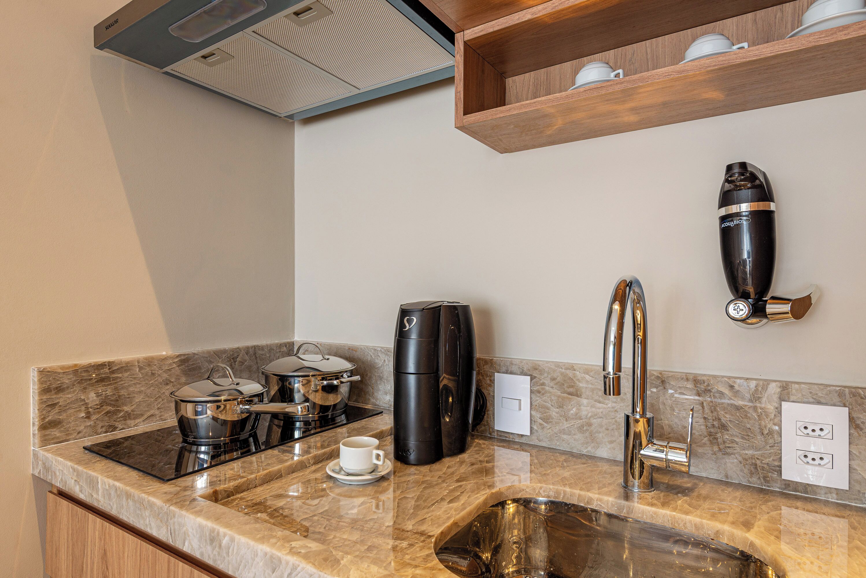 A modern kitchen with a marble countertop, a coffee maker, a kettle, and a sink.