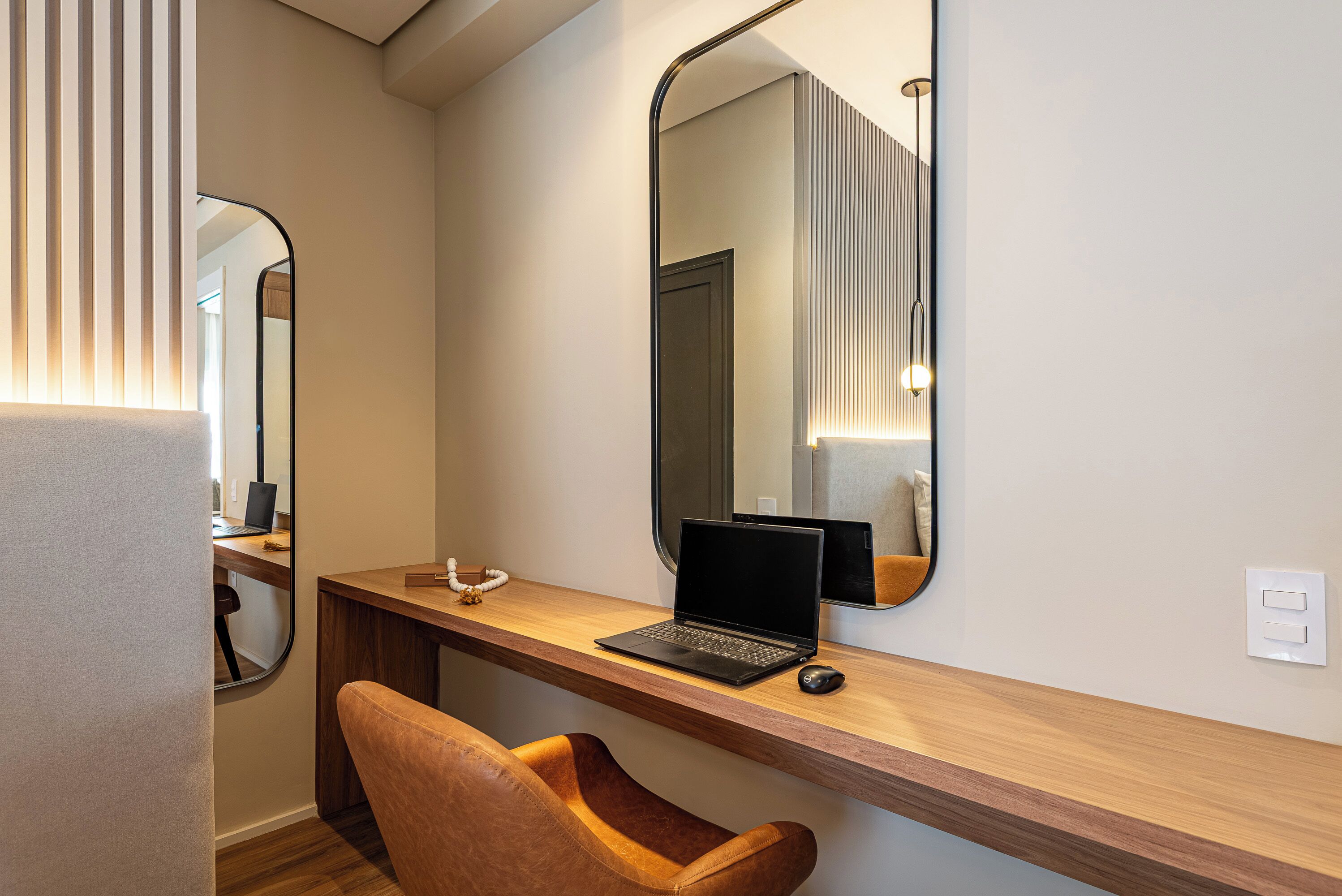A modern room with a wooden desk, a laptop, a chair, and a large mirror.