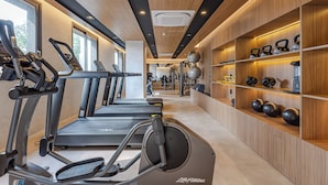 Une salle de sport équipée de tapis de course, de vélos d’exercice et de kettlebells, avec des murs en bois et de grandes fenêtres.