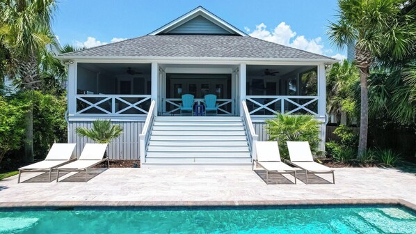 A house with a covered porch, a swimming pool, and two lounge chairs.
