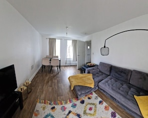 Un salon comprenant un canapé, un téléviseur, un coin repas avec des chaises et un coin cuisine avec une table et un comptoir.