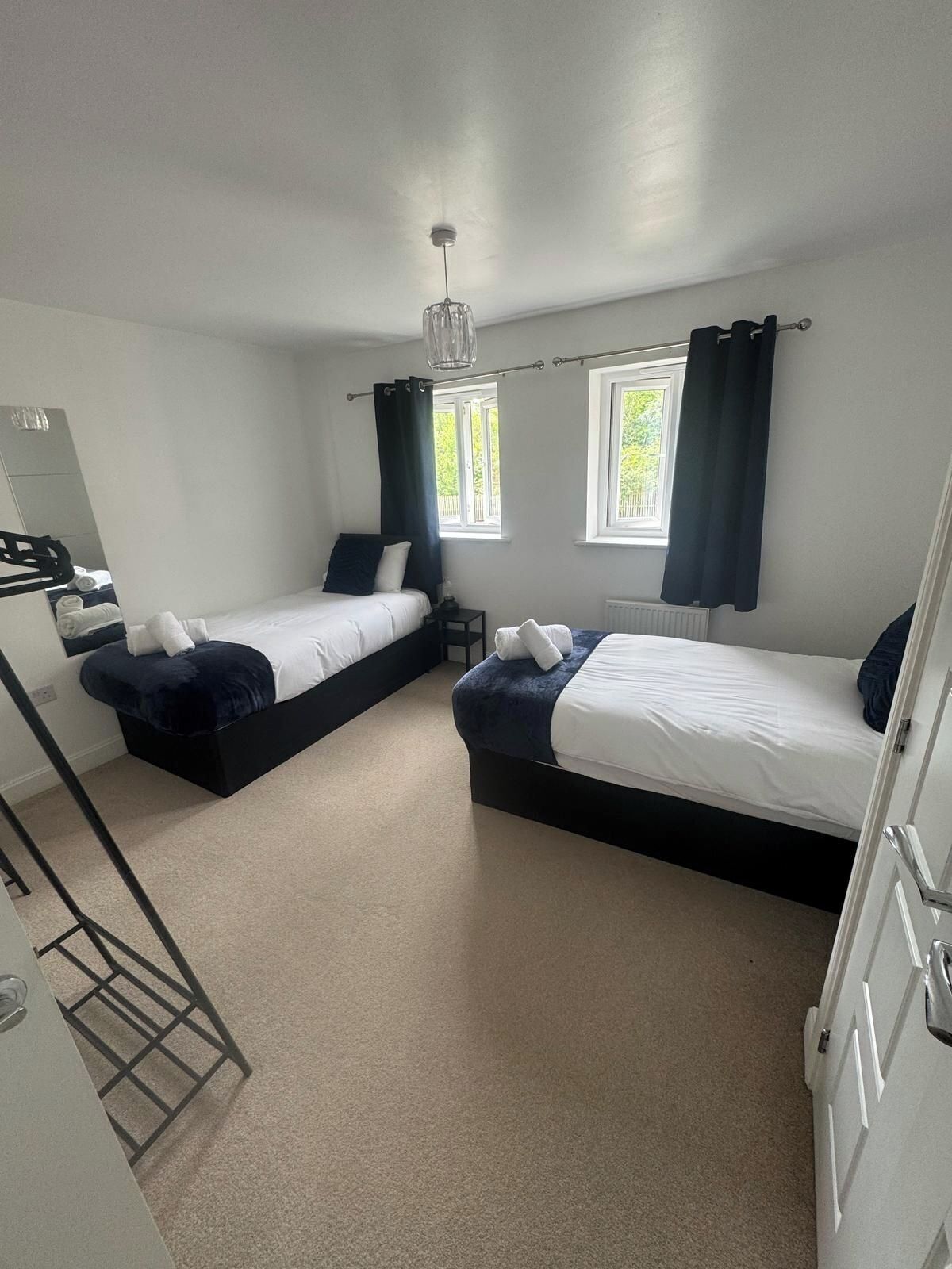 A hotel room with two beds, a mirror, a radiator, and a window with curtains.