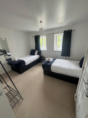 A hotel room with two beds, a mirror, a radiator, and a window with curtains.