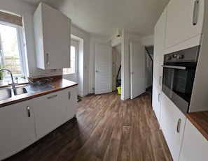 Une cuisine avec des armoires blanches, un plan de travail en bois et un four encastré.