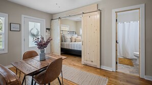 A room with a wooden dining table, chairs, a ceiling fan, and a bed with a wooden door. - Precious 1-bedroom Cottage in Midtown Mobile Recently renovated with fenced yard (Mobile)
