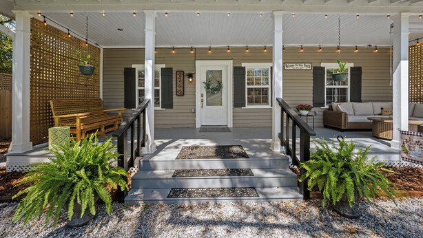 A covered porch with a bench, potted plants, and a welcome sign. - Precious 1-bedroom Cottage in Midtown Mobile Recently renovated with fenced yard (Mobile)