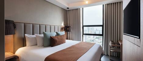 A modern hotel room with a large bed, a flat-screen TV, a city view, and a wooden nightstand.