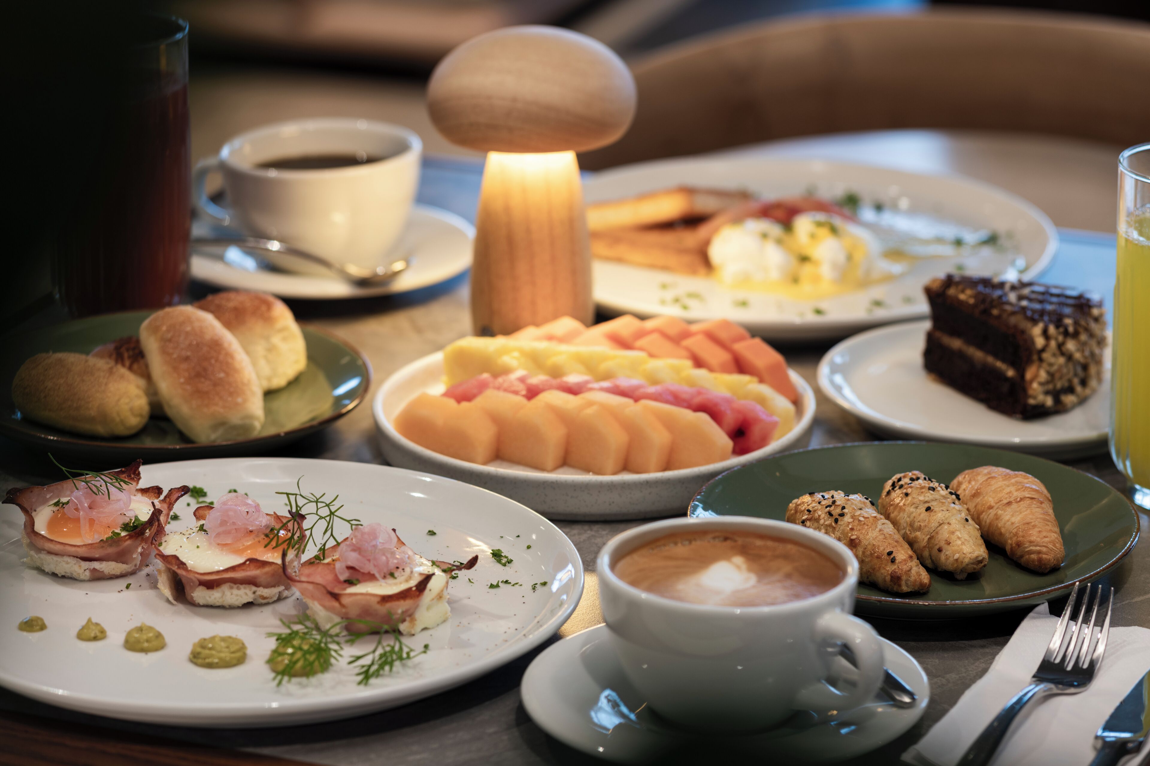 A breakfast setting with various dishes, including pastries, a hot beverage, and a fruit plate.