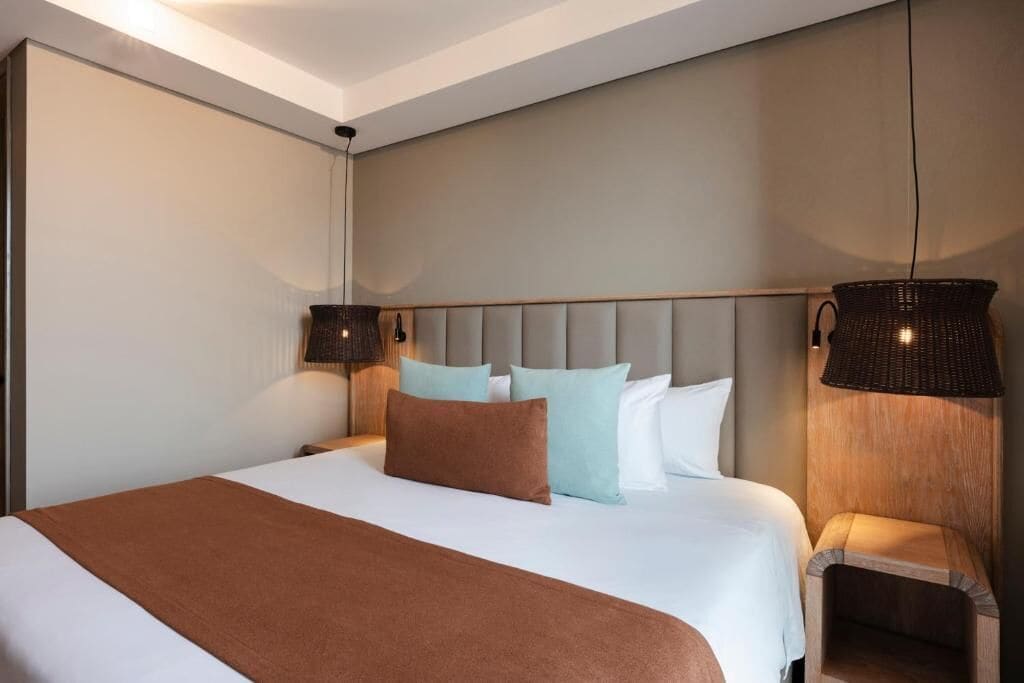 A modern hotel room with a large bed, a headboard, and two wall-mounted lamps.