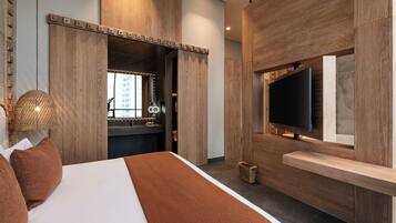A modern hotel room with a large bed, a TV mounted on a wooden panel, and a bathroom visible through a wooden door.