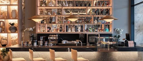 Una zona de bar con encimera de mármol, taburetes de madera y una pared llena de botellas de licores.