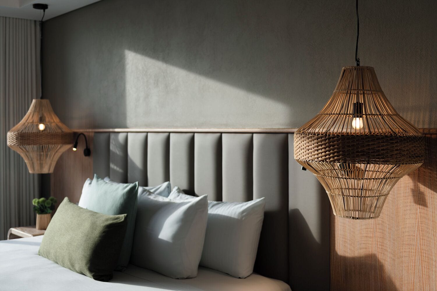 Un dormitorio moderno con cabecera capitonada, cama con múltiples almohadas y dos lámparas colgantes tejidas.