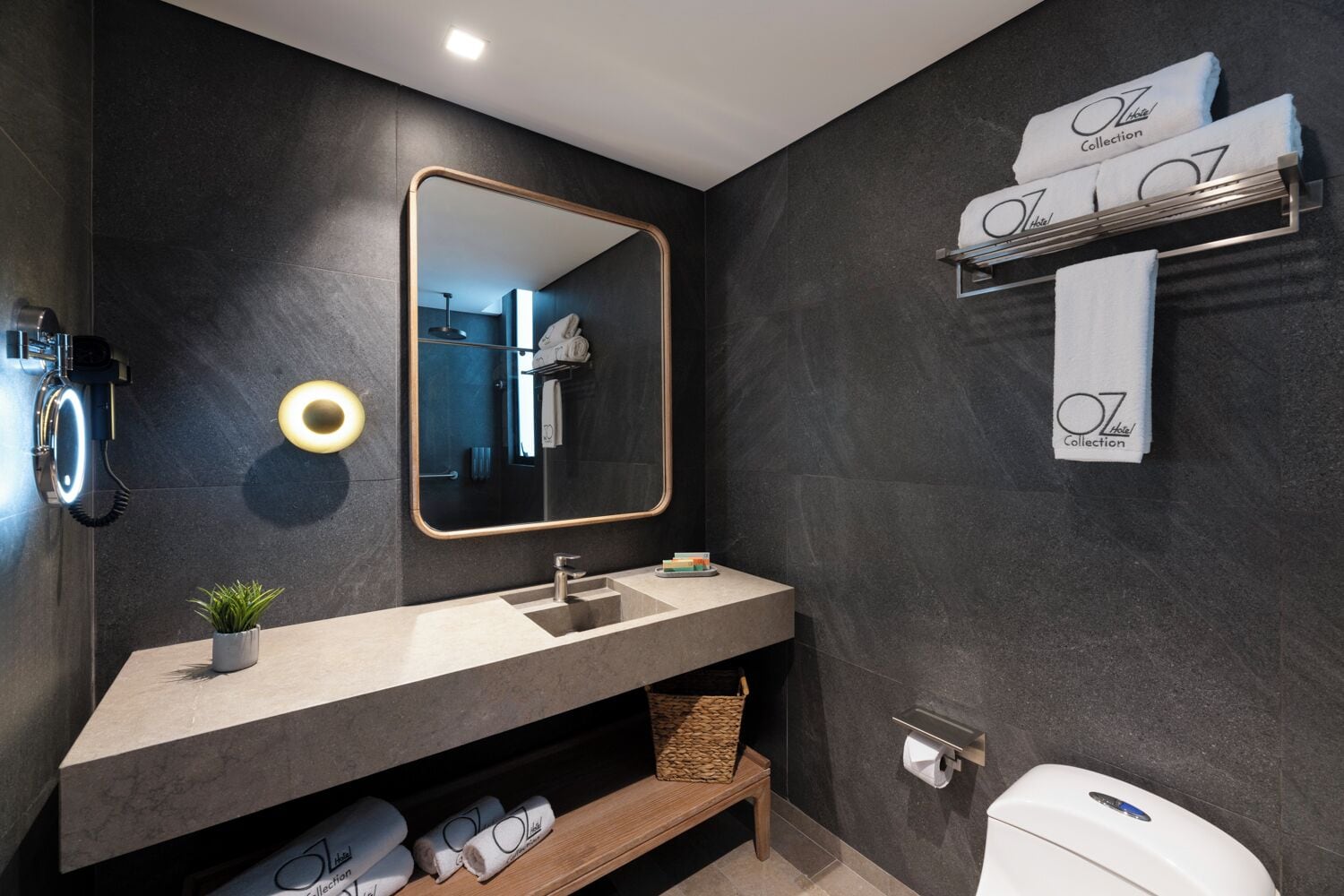 Un baño moderno con una pared oscura, un espejo grande, un lavabo, un perchero para toallas y un inodoro.