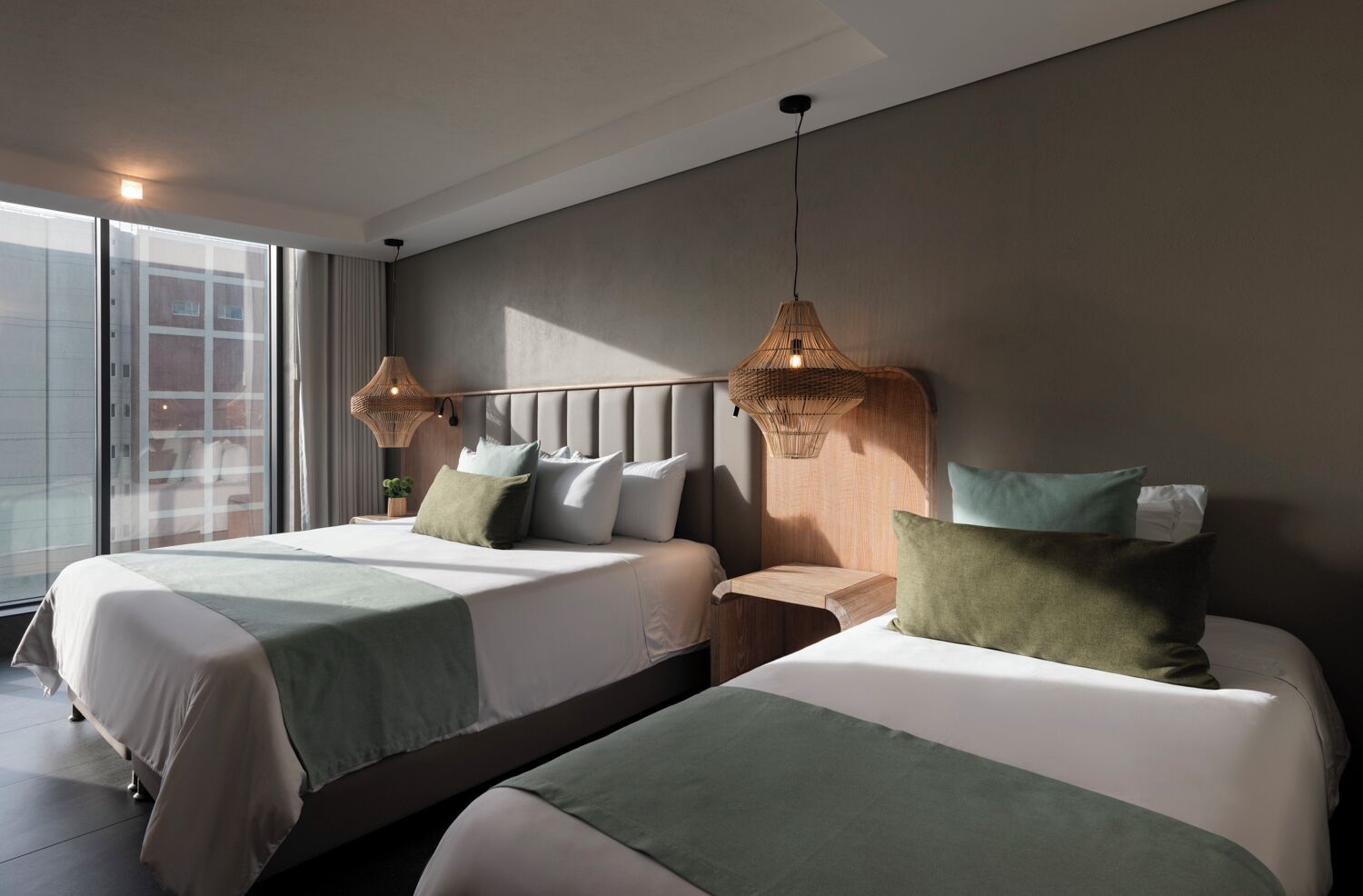 A modern hotel room with two beds, a large window, and a view of the city.
