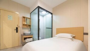Une chambre d’hôtel comprenant un lit, une armoire, une salle de bain avec une porte en verre et une étagère avec des serviettes.