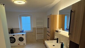 Una cocina compacta con lavadora integrada, un lavamanos con espejo y una ventana.
