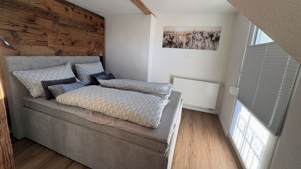 Un dormitorio moderno con cabecera de madera, cama grande con ropa de cama estampada, radiador y ventana con persianas.