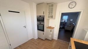 Una cocina compacta con electrodomésticos integrados, una zona de comedor con mesa y sillas, y una sala de estar con sofá y lámpara.