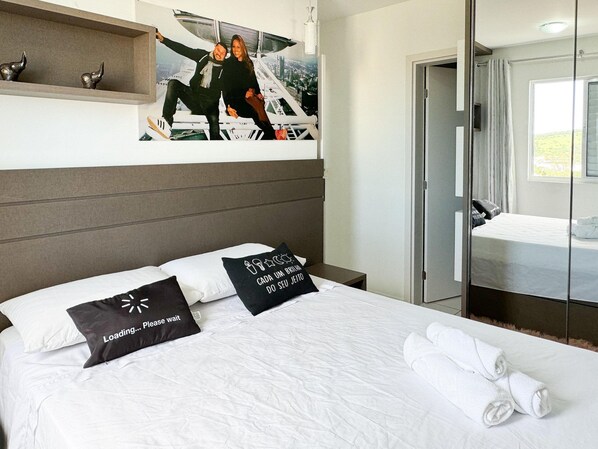 Une chambre d’hôtel avec un lit, des oreillers, une tête de lit, une table de chevet, un miroir, une fenêtre et une porte.