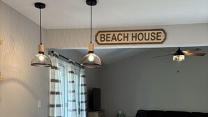 Cuina amb taulell blanc, dues làmpades penjants, ventilador de sostre i un cartell que diu "BEACH HOUSE".
