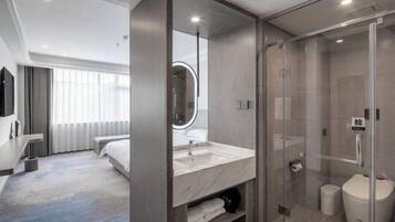 A modern hotel room with a large bed, a bathroom with a glass shower enclosure, and a large mirror.