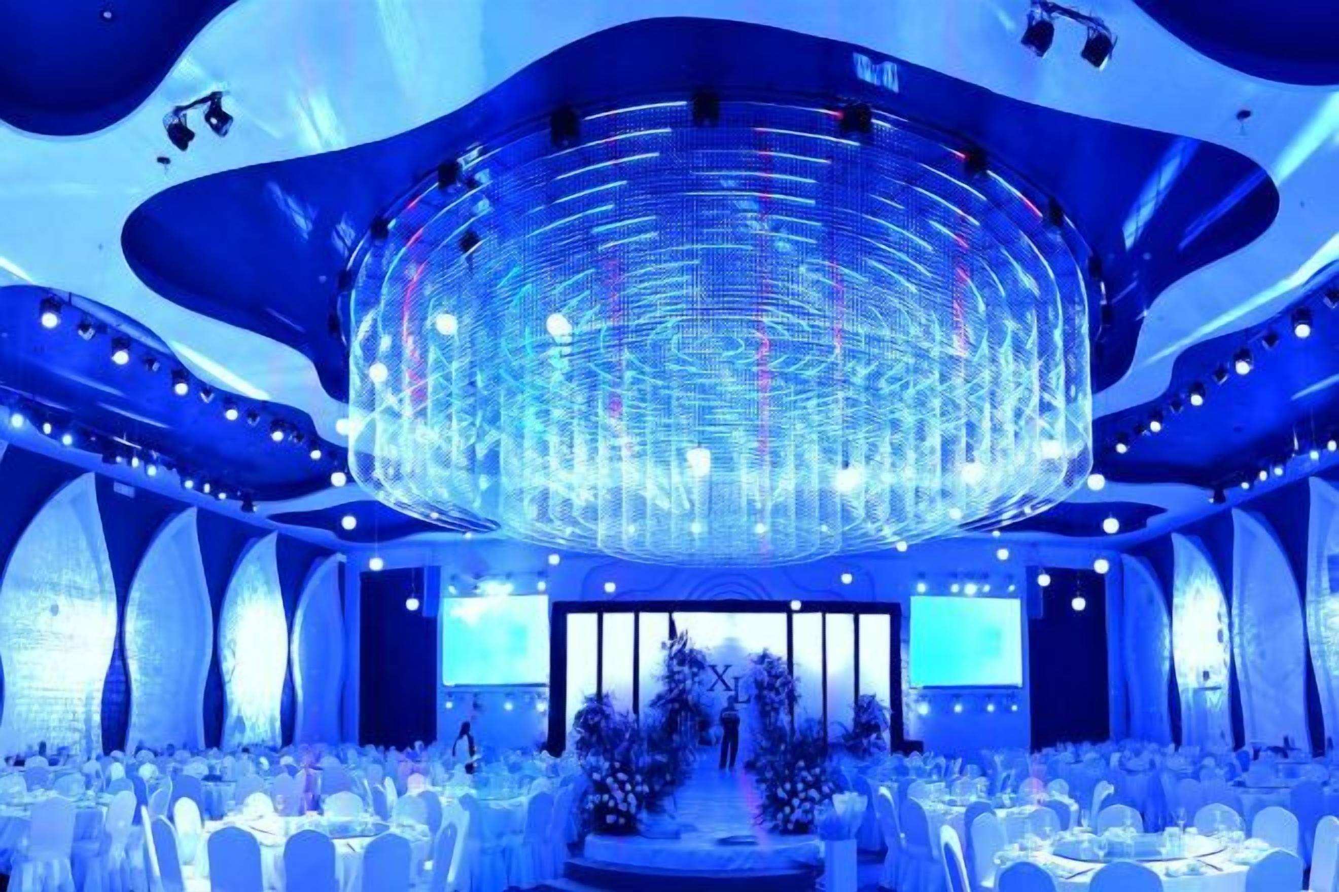 A large, circular chandelier in a banquet hall with white tables and chairs.