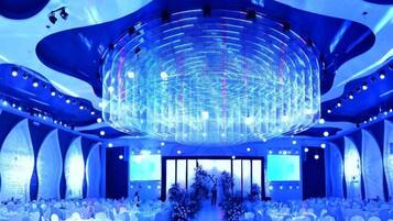 A large, circular chandelier in a banquet hall with white tables and chairs.