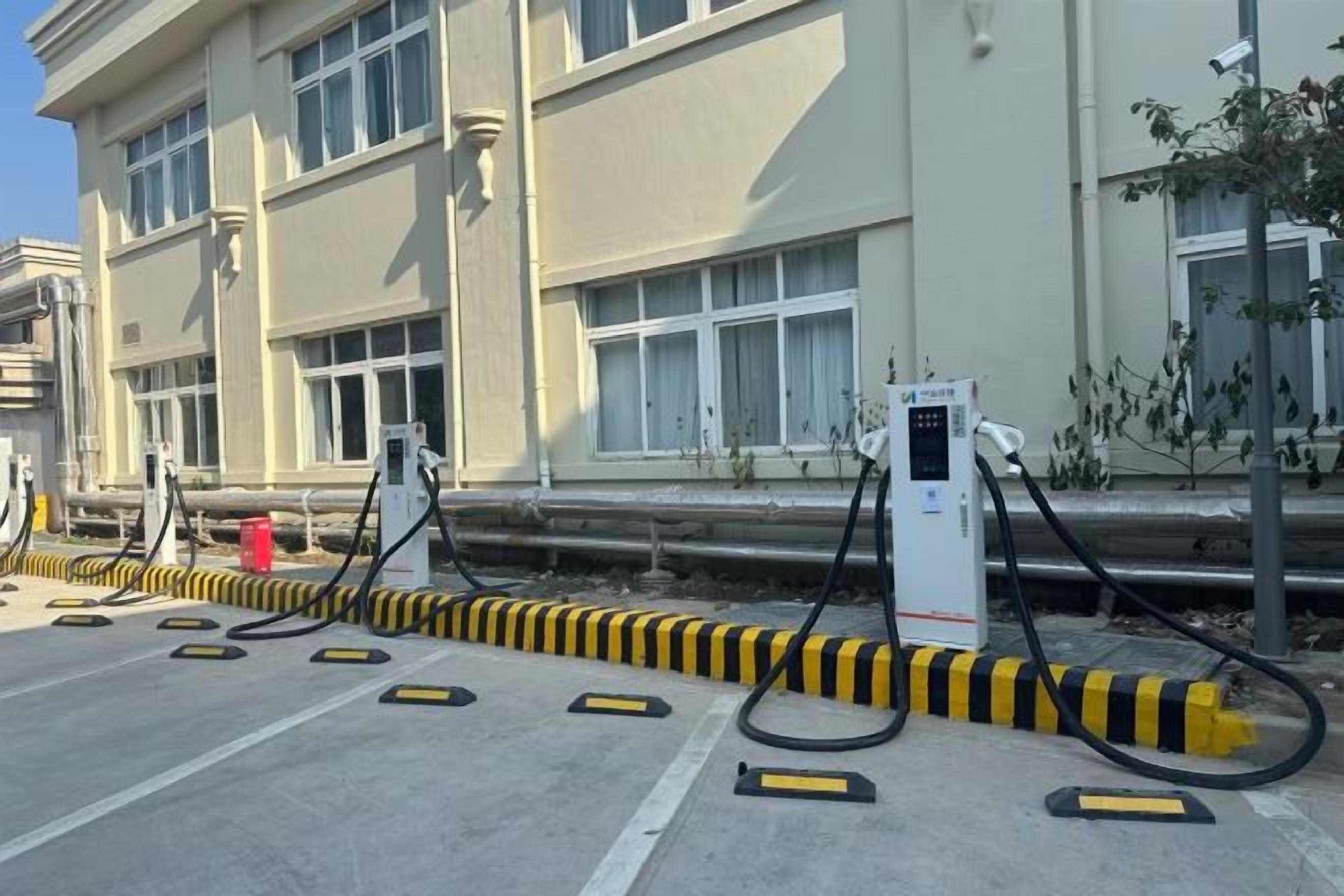 A parking area with electric vehicle charging stations, a building with windows, and a curb.