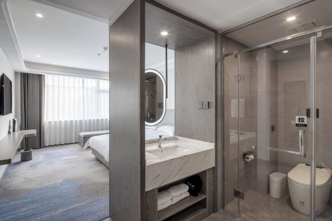 A modern hotel room with a large bed, a bathroom with a glass shower enclosure, and a large mirror.