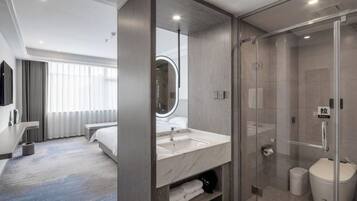 A modern hotel room with a large bed, a bathroom with a glass shower enclosure, and a large mirror.