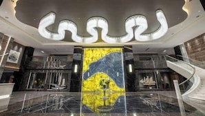 Un vestíbulo moderno con suelo de mármol, una obra de arte central y una escalera.