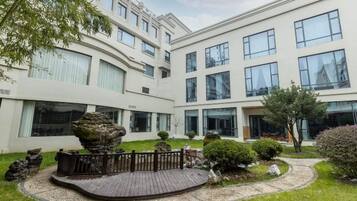 A modern building with multiple floors, large windows, and a landscaped garden with a wooden deck and rock formations.
