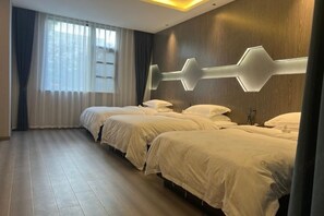 Camera d'albergo con tre letti allineati lungo una parete, illuminata da un lampadario geometrico.