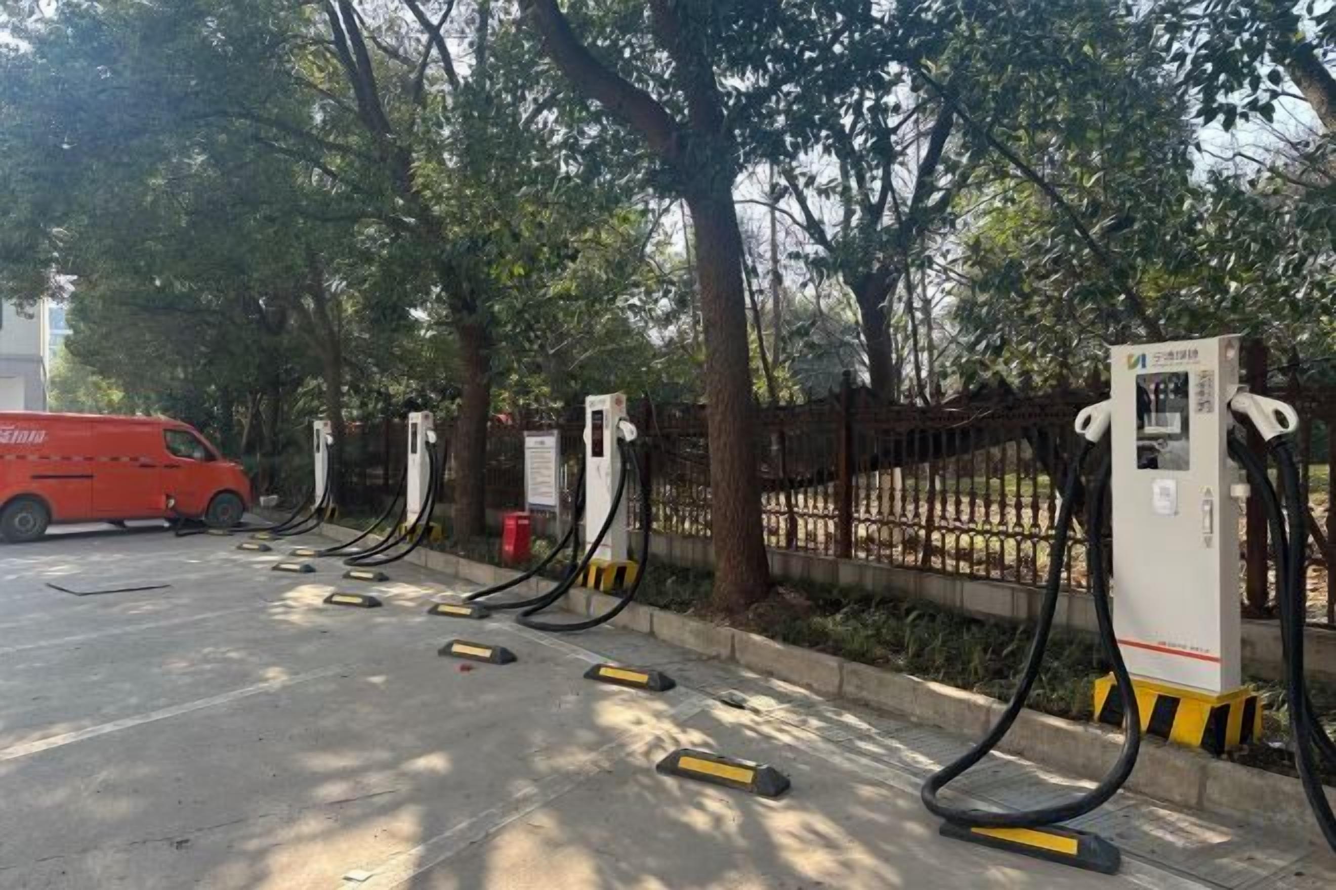 A fuel station with multiple pumps, a red van, and a fence with trees in the background.