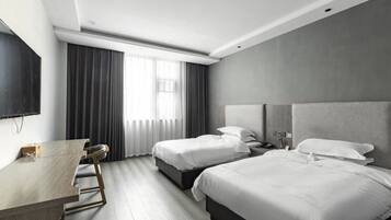 A hotel room with two beds, a desk, a flat-screen TV, and a window with curtains.