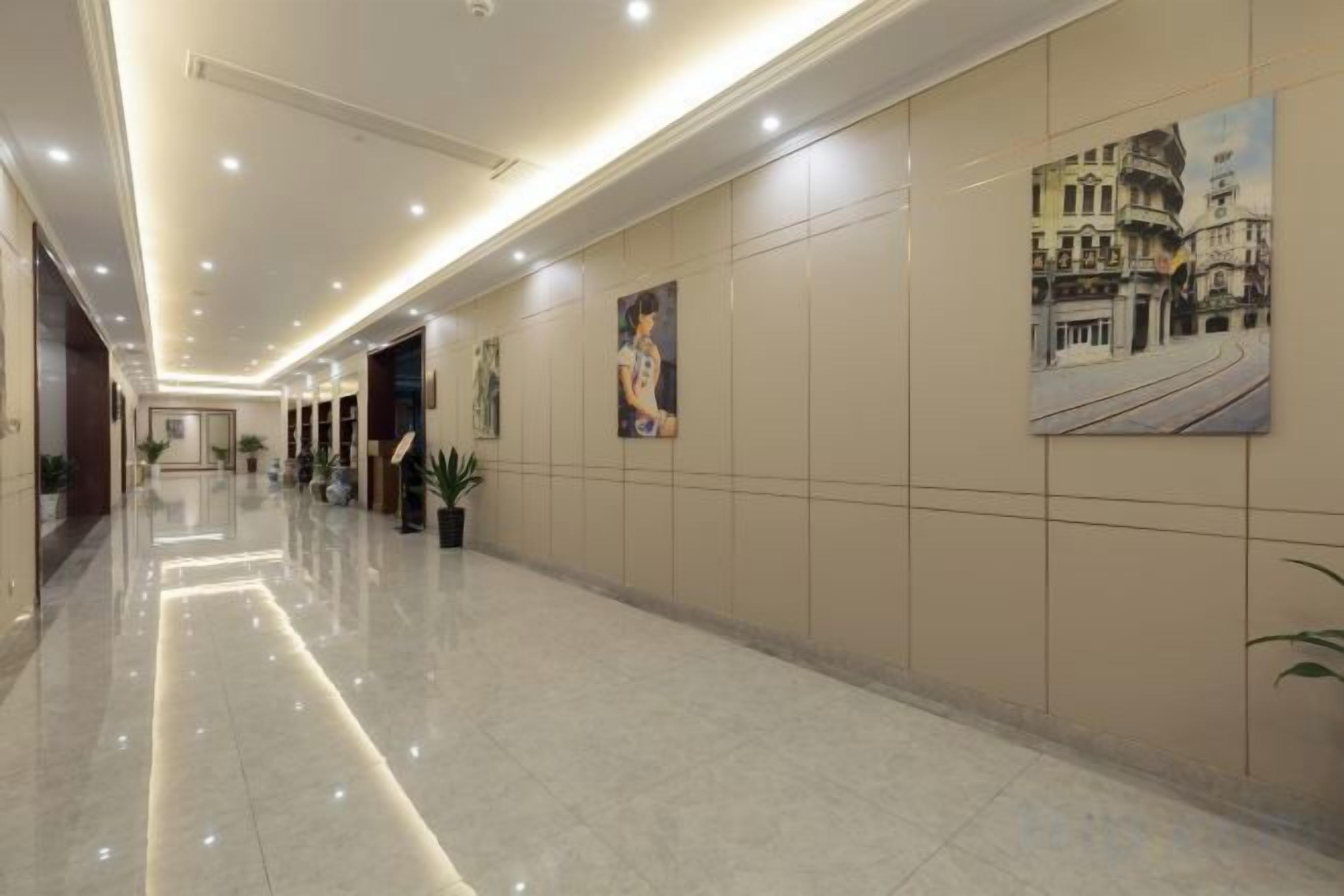 A hotel corridor with a polished floor, wall-mounted artwork, and recessed lighting.
