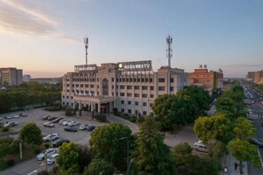 A multi-story building with a central entrance, surrounded by trees and parked cars. - Xiang Yuan Hotel (Cixi)